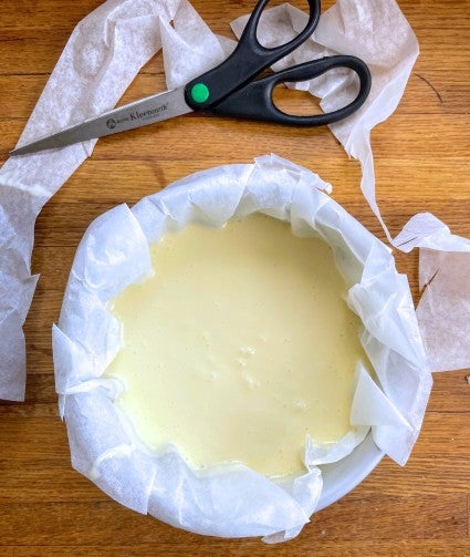 6" x 2" round cake pan lined with parchment and filled with cheesecake batter, ready to be baked in an air fryer.