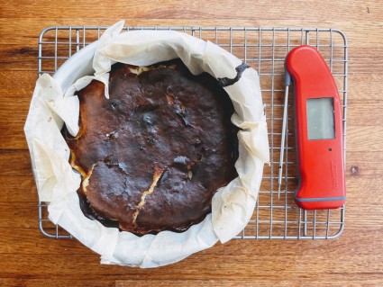 Baked Basque-style cheesecake on a cooling rack next to a Thermapen digital thermometer.