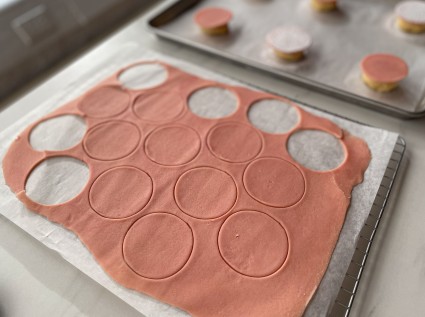 A pink sheet of dough rolled and cut for cookie caps