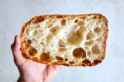Hand holding a  loaf of Pan de Cristal cut to show its holey interior.