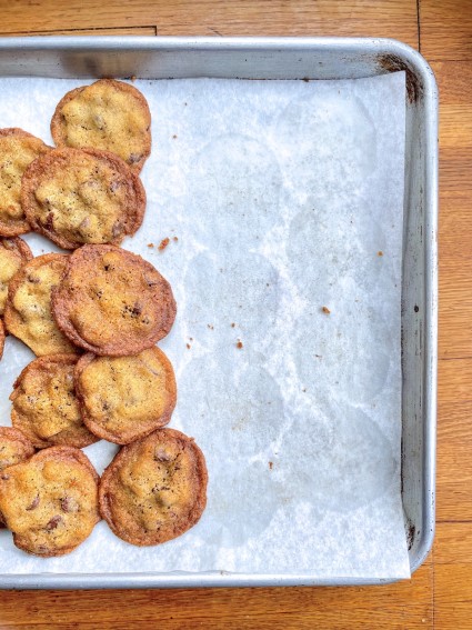 Chocolate chip cookies on one side of a piece of parchment on a sheet pan; bare parchment showing grease rings where the cookies baked.