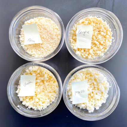 Four small bowls of grated cheese, four different varieties.