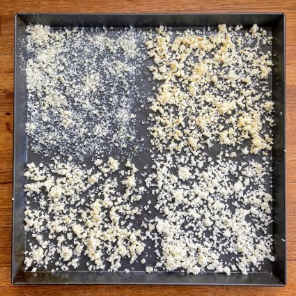 Square black pizza pan sprinkled with four different cheeses in four different quadrants.