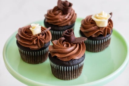 Chocolate cupcakes on a cake stand topped with white and dark chocolate roses made from modeling chocolate