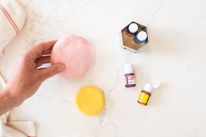 Two disks of modeling chocolate, one in pink and one in yellow, next to two bottles of natural food dye