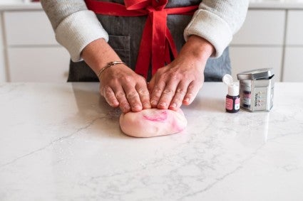 A baker kneading in natural food dye into a log of modeling chocolate