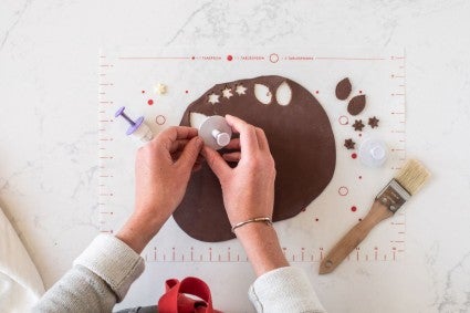 A baker using popout cutters to make leaves and small flowers from a sheet of rolled out modeling chocolate