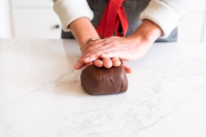 A baker kneading a log of modeling chocolate on a marble surface