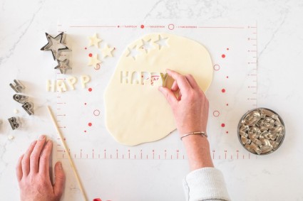 A baker cutting out the word "happy" using letter cutters from a rolled out piece of modeling chocolate