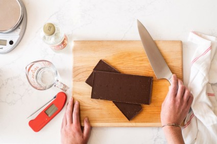 Two large bars of chocolate on a cutting board with a thermometer, knife, and scale