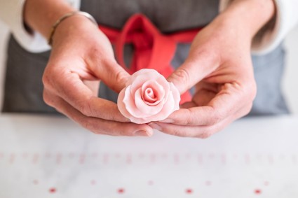 A baker holding a pink rose made out of modeling chocolate