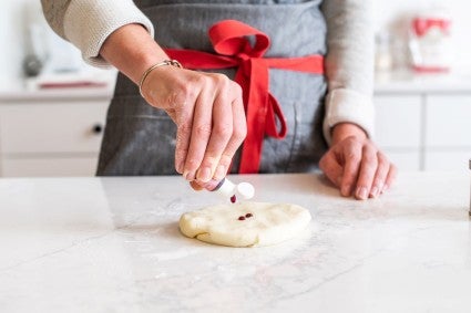 A baker adding a few drops of natural food dye to a disk of white modeling chocolate