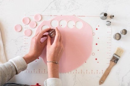 A baker cutting out rounds from a rolled out sheet of pink modeling chocolate