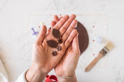 A baker holding up leaves and small flowers made from modeling chocolate