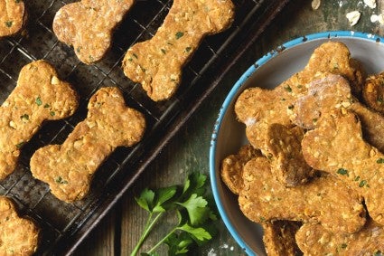 Baked bone-shaped dog biscuits, some on a pan, some on a plate.