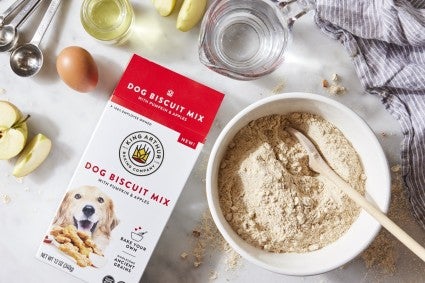 Box of dog biscuit mix on a table with bowl and ingredients.