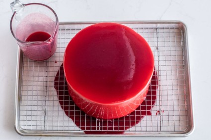 A cake resting on a cooling rack after it was just coated in raspberry glaze