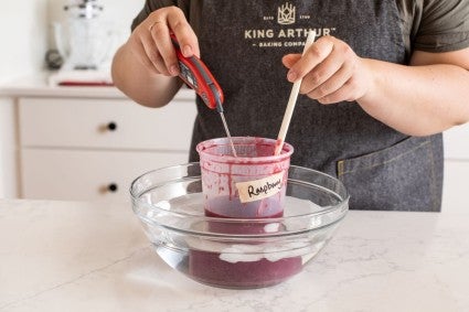 A baker cooling a container of mirror glaze in an ice water bath