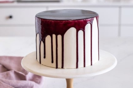 A cake decorated with a crown of drips of blueberry mirror glaze