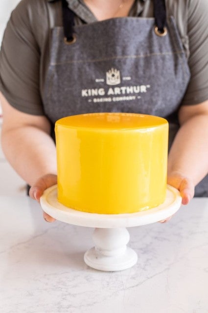 A baker presenting a cake finished with mango mirror glaze