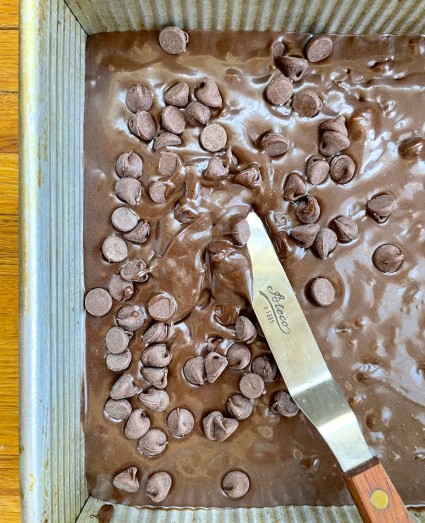 Chocolate chips being gently stirred into brownie batter in a pan. 