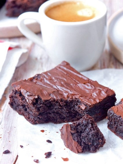 Brownie square on a plate, bite taken out, cup of coffee in the background.