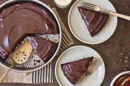 Round single-layer chocolate-frosted chocolate cake in a pan, slices cut out and plated.