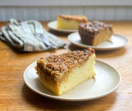 Wedge of coconut-topped Lazy Daisy Cake on a plate, other cake wedges in the background.