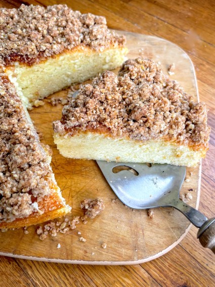 Crumb-topped coffeecake on a cutting board, one wedge cut out.