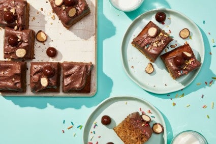 Slices of banana snacking cake with chocolate malted frosting on a platter and plates