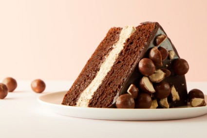 A slice of malted chocolate layer cake on a plate with malted milk balls