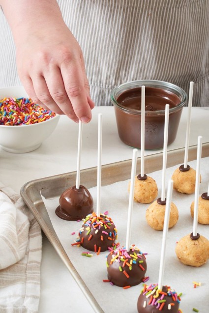 Hands dipping cake pops in chocolate coating