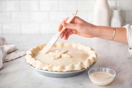 Baker using pastry brush to brush soy milk on unbaked pie