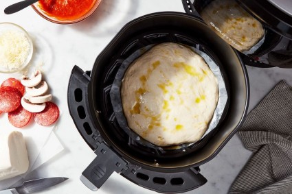 Shaped pizza crust on a round of parchment, drizzled with oil and placed in an air fryer bucket to bake.