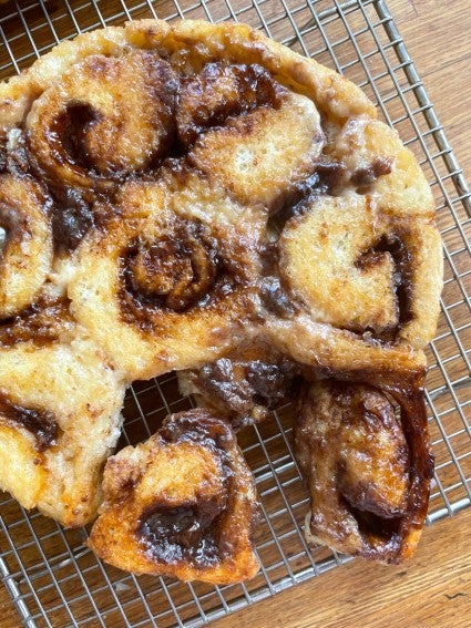 Cream-soaked cinnamon rolls baked and turned out onto a cooling rack.