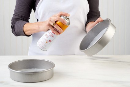 Round cake pans, lined with parchment, being sprayed with nonstick vegetable oil spray.