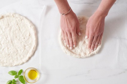 Hands shaping gluten-free pizza crust into a round