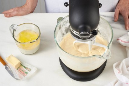 Cake batter in stand mixer, with measuring cup of hot milk and butter next to it