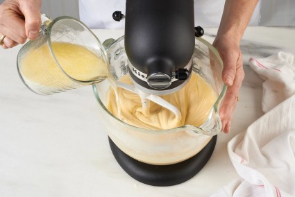 Hot milk being poured into stand mixer full of cake batter