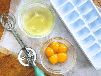 A bowl of egg whites and a bowl of egg yolks, with broken egg shells and a whisk on the side.