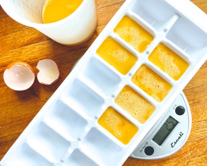Beaten eggs poured into an ice cube tray, sitting on an electronic scale.