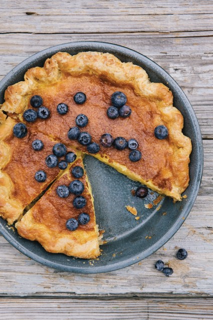 Buttermilk Pie garnished with blueberries, with a slice taken out.