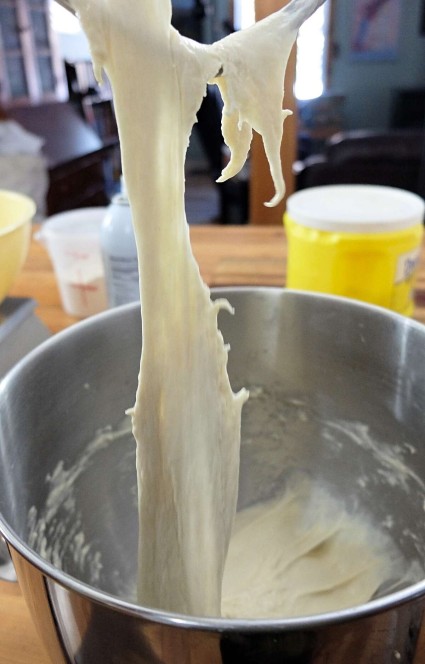 After being kneaded in a KitchenAid stand mixer, dough stretching from the dough hook to the bowl