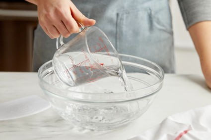 Baker pouring water into mixing bowl