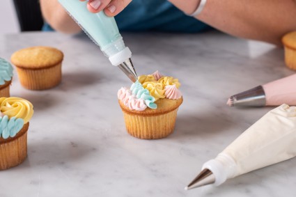 A baker piping a cupcake with different designs 