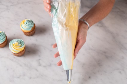 A baker holding a pastry bag filled with three different colors of frosting