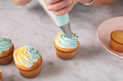 A baker piping frosting onto a cupcake with multicolored frosting