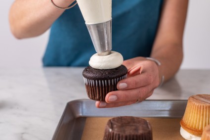 A baker piping buttercream on top of a cupcake with a pastry bag