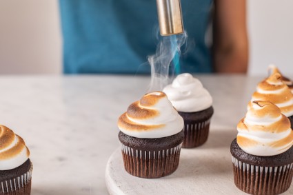 A baker using a torch to toast meringue-frosted cupcakes