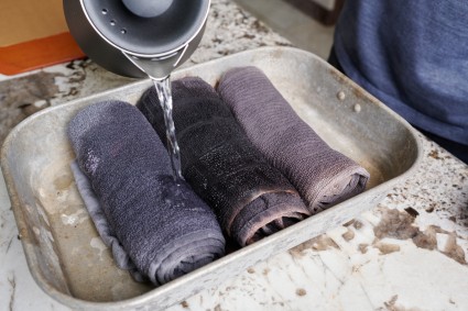 Pouring water over rolled towels in baking pan